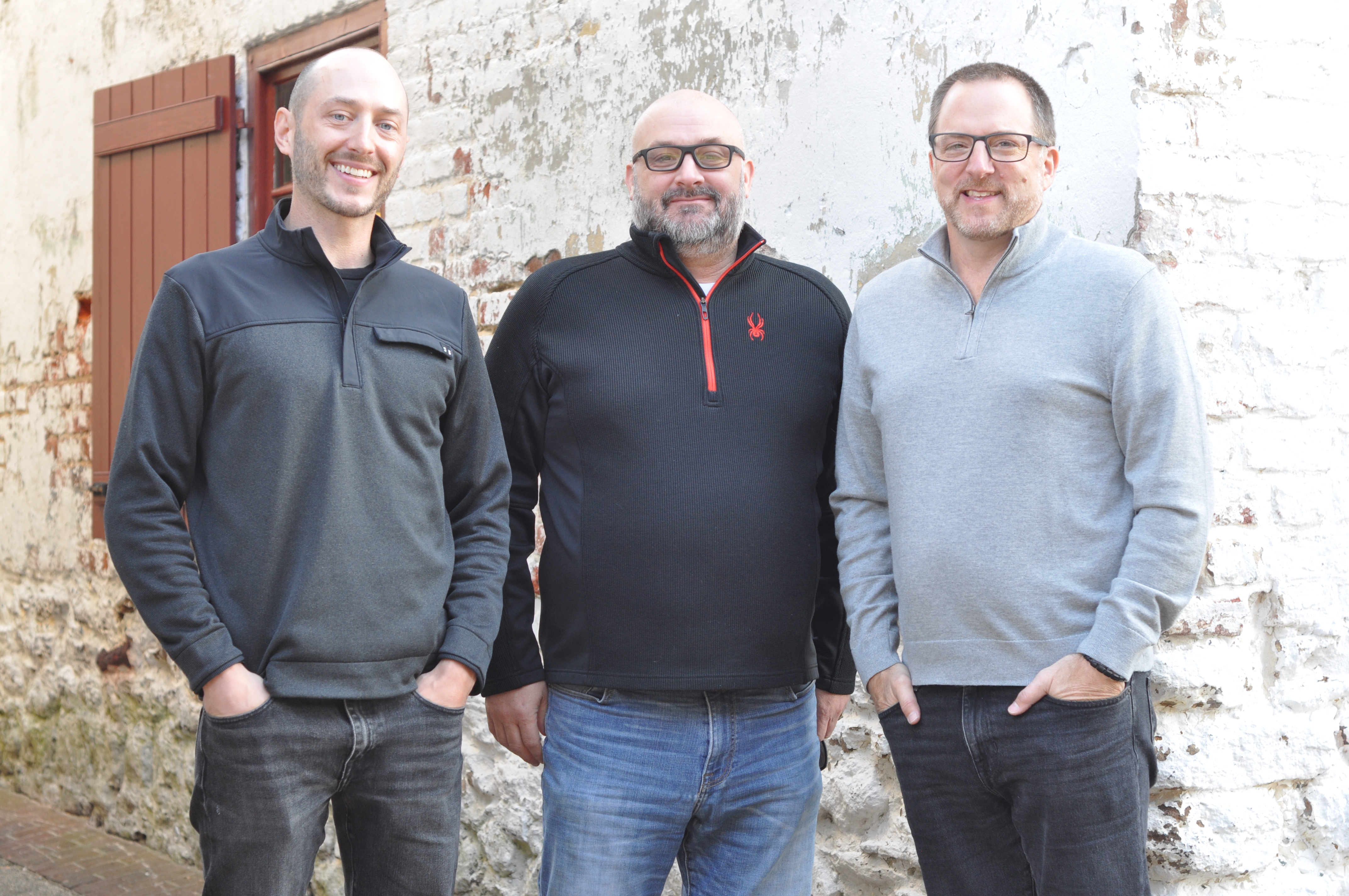 Three men posing in front of a stone wall home