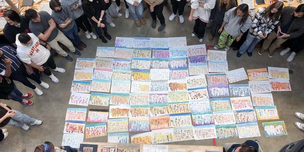 Students standing around multiple Lucien Steil style drawings of buildings, in the Great Space. 