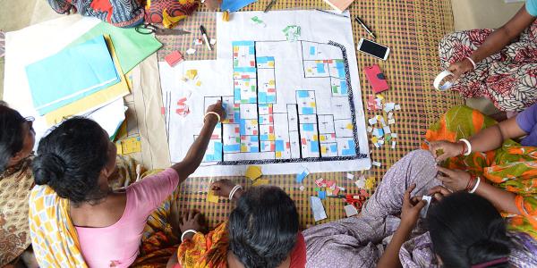 Children sitting on the ground pointing at a community plan