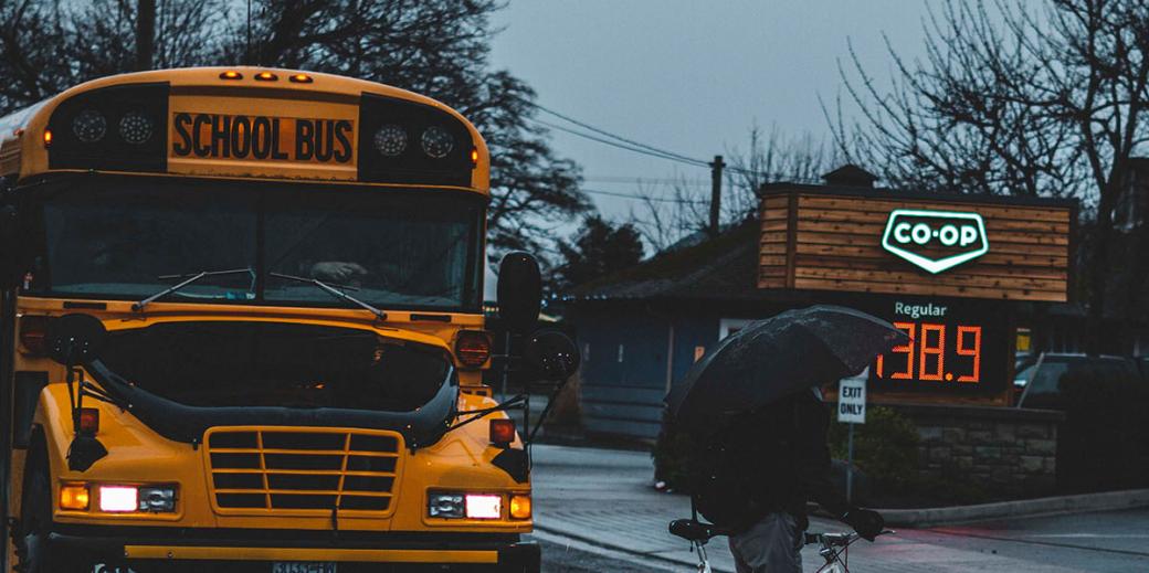 School bus stopped and a person on the crosswalk with a bike and umbrell.