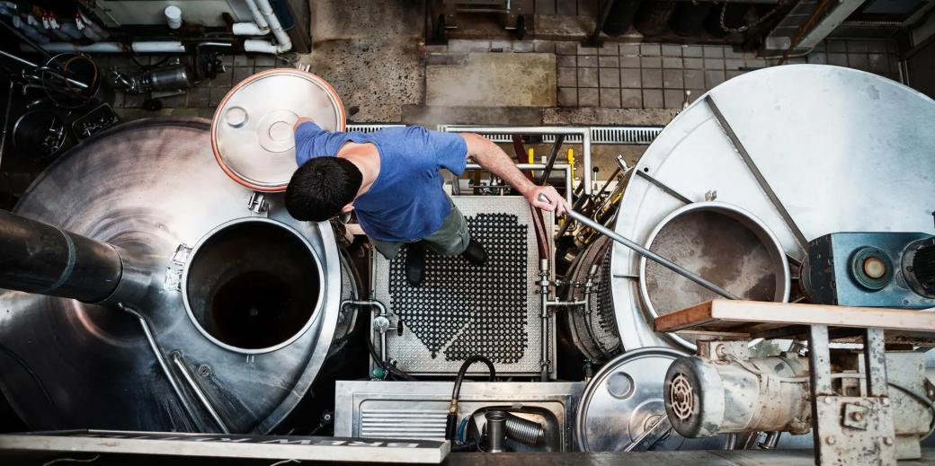 Top view of a man looking into a beer fermenting tank while stirring another.