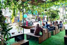 People sitting on wooden tables at a beer garden looking at cars on street