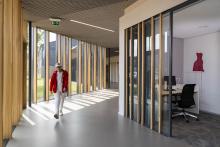 Man walking through a naturally lit hallway inside a building with tall windows and wooden structures.