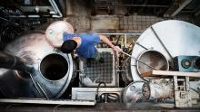 Top view of a man looking into a beer fermenting tank while stirring another.