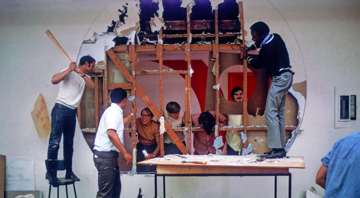 Students from class of '72 standing by a large hole in the wall.