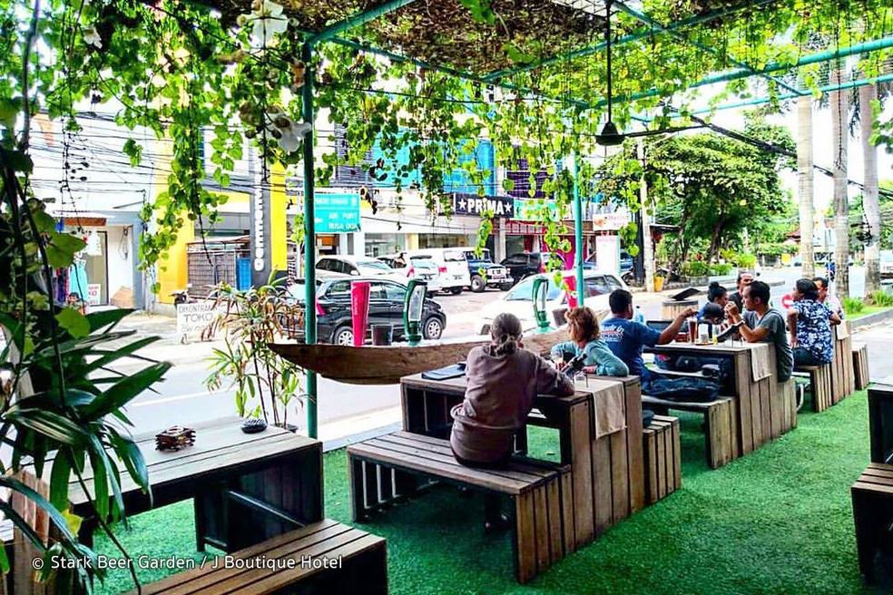 People sitting on wooden tables at a beer garden looking at cars on street