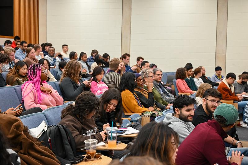 People in an auditorium and a girl with bright pink hair and sweater stands out