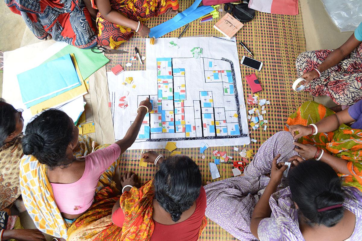 Children sitting on the ground pointing at a community plan