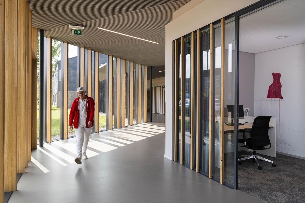 Man walking through a naturally lit hallway inside a building with tall windows and wooden structures.