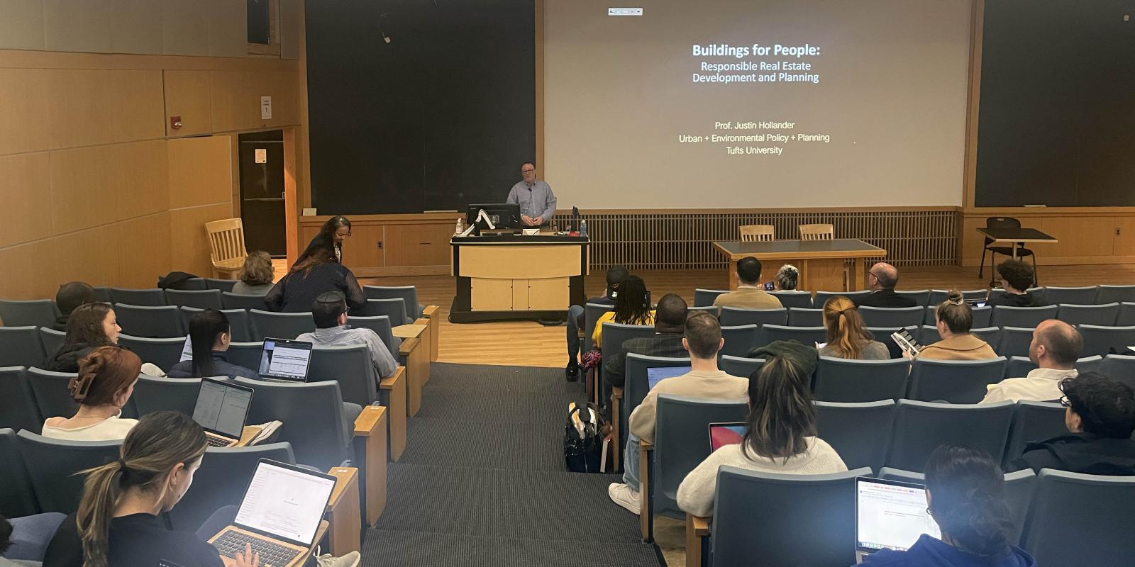 A person presenting a lecture in an auditorium filled with students